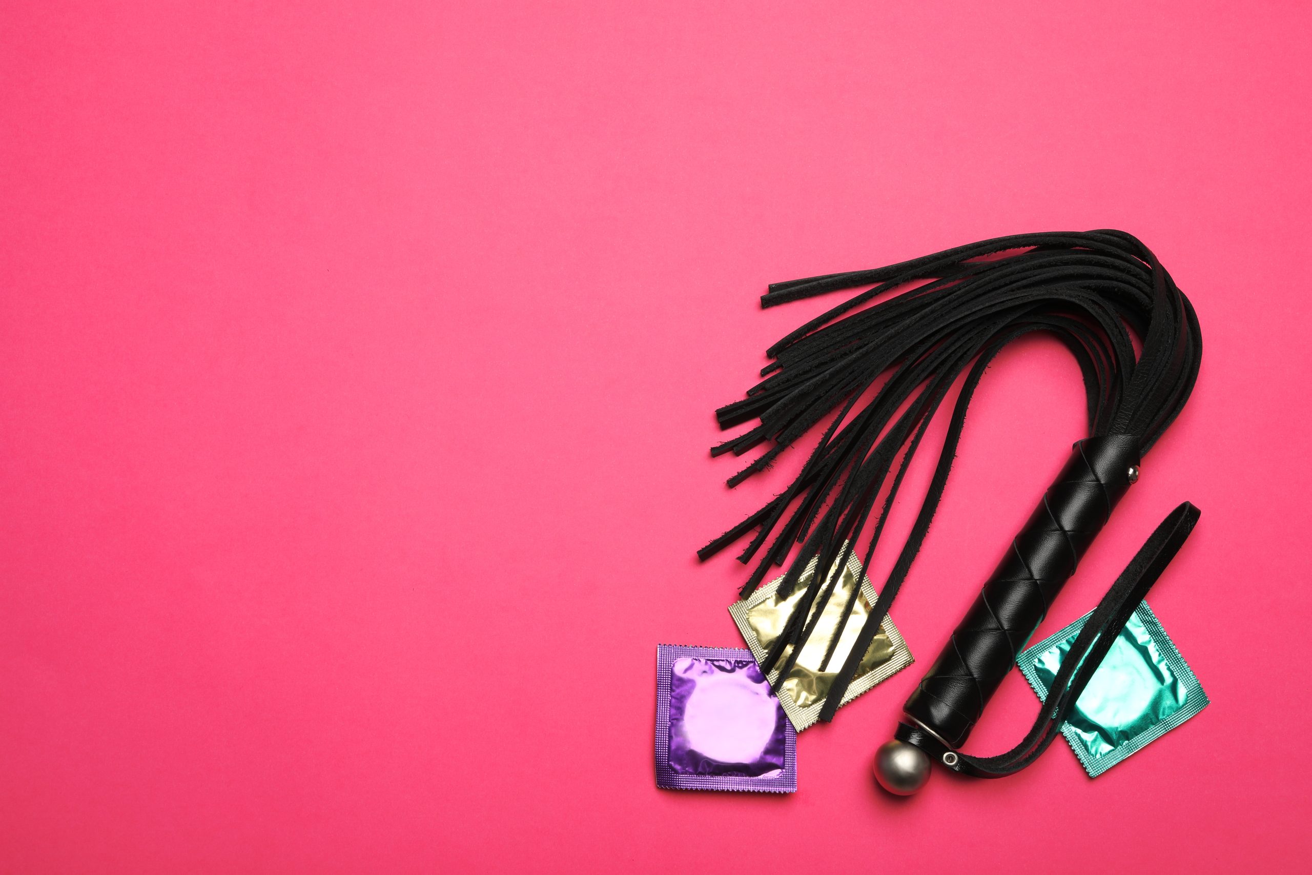 Whip and condoms on pink background, top view with space for text. Sex game